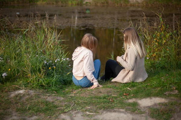 Flickorna sitter på stranden av sjön. Kvinnor vilar i naturen. Planera bakifrån. Flickor njuter av varmt väder på hösten. — Stockfoto