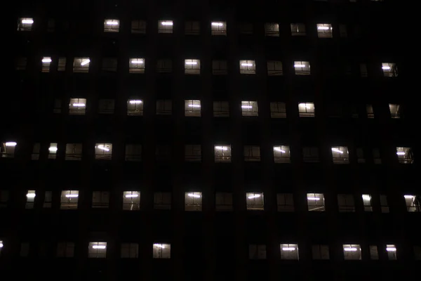 Die Fenster des Gebäudes brennen im Dunkeln. Ein sich wiederholendes architektonisches Element des Fensters. Die Textur der glühenden Öffnungen. Hochhaus in der Nacht. — Stockfoto