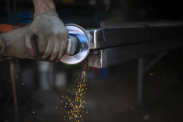 Grinding metal with a grinder. Working in a metal processing workshop. Cleaning the steel seam. The man works with an electric tool. Sparks from metal heating. — Stock Photo, Image