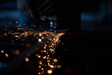 Öğütücüyle öğütülmüş metal. Metal işleme atölyesinde çalışıyorum. Çelik dikişleri temizliyorum. Adam elektrikli bir aletle çalışıyor. Metal ısıtmadan kıvılcımlar.