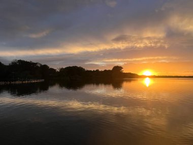 Yaz günbatımı manzarası Norfolk 'un üzerinde batıyor İngiltere' nin sakin suları, güzel turuncu mavi gökyüzü, yelkenliden ufka kadar seyrediliyor ağaçlar, sazlıklar, bulutlar yansıyor 