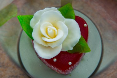 Kırmızı marmelat kalbine yeşil yaprakları ile beyaz gül. Aşıklar ve düğünler için lezzetli tatlılar.