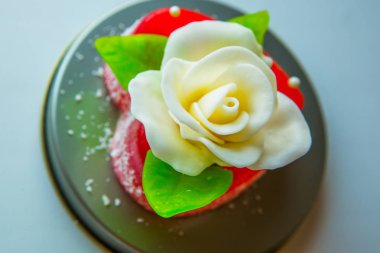 Kırmızı marmelat kalbine yeşil yaprakları ile beyaz gül. Aşıklar ve düğünler için lezzetli tatlılar.