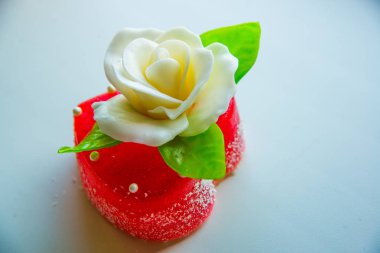 Kırmızı marmelat kalbine yeşil yaprakları ile beyaz gül. Aşıklar ve düğünler için lezzetli tatlılar.