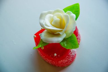 Kırmızı marmelat kalbine yeşil yaprakları ile beyaz gül. Aşıklar ve düğünler için lezzetli tatlılar.