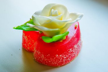 Kırmızı marmelat kalbine yeşil yaprakları ile beyaz gül. Aşıklar ve düğünler için lezzetli tatlılar.