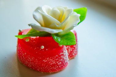 Kırmızı marmelat kalbine yeşil yaprakları ile beyaz gül. Aşıklar ve düğünler için lezzetli tatlılar.