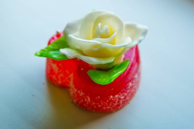 Kırmızı marmelat kalbine yeşil yaprakları ile beyaz gül. Aşıklar ve düğünler için lezzetli tatlılar.