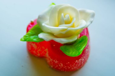 Kırmızı marmelat kalbine yeşil yaprakları ile beyaz gül. Aşıklar ve düğünler için lezzetli tatlılar.