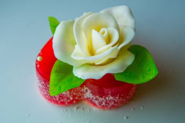 Kırmızı marmelat kalbine yeşil yaprakları ile beyaz gül. Aşıklar ve düğünler için lezzetli tatlılar.