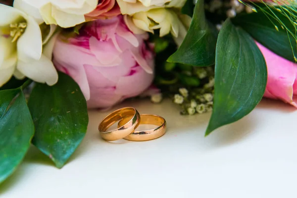 Två guld vigselringar ligga nära en bukett blommor till bruden. — Stockfoto