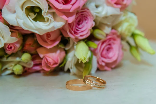 Anello d'oro nuziale. Romantico fidanzamento due anelli di diamanti sono vicino al bouquet sposa di rose rosa e fiori bianchi — Foto Stock