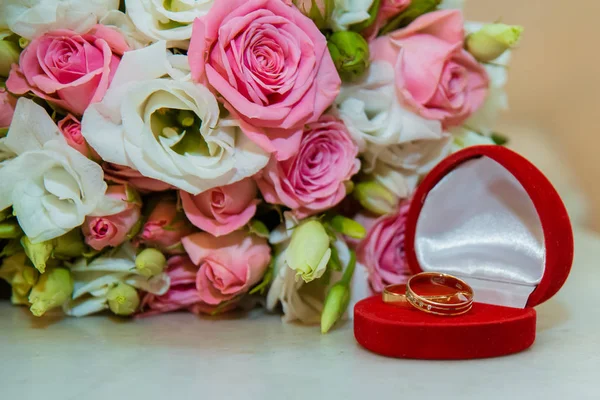 Guld vigselring. Romantiska engagemang två diamantringar är i en röd ruta i form av ett hjärta, de ligger nära en bukett av nevetas av rosa rosor och vita blommor — Stockfoto