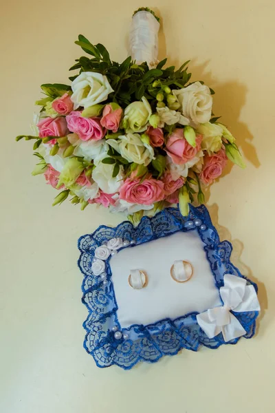 Obrączkę. Romantyczne zaręczyny, dwa złote pierścienie są na poduszce z koronki niebieski, pierścienie są w pobliżu narzeczonych bukiet róż różowy i biały — Zdjęcie stockowe