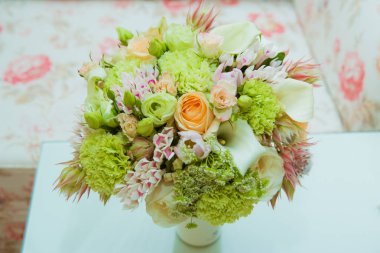 Güzel bir gelin buketi hassas tondan yeşil, pembe, turuncu ve beyaz çiçekler düğün gününde bir vazoda var.