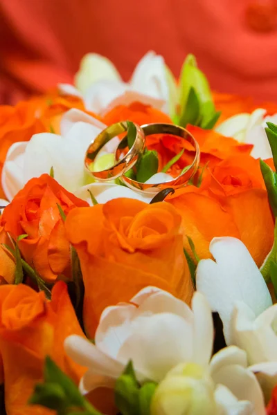 结婚戒指两个金色的复古戒指和一束橙色玫瑰和白色花朵的新娘花束 — 图库照片