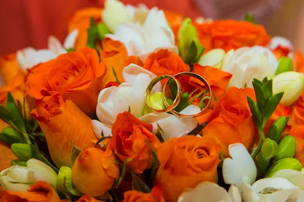 结婚戒指两个金色的复古戒指和一束橙色玫瑰和白色花朵的新娘花束 — 图库照片