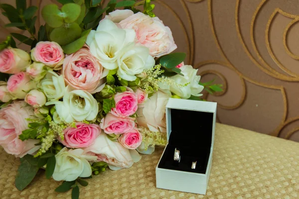 Vigselring i vitt guld. Två platina ringar av bruden och brudgummen i en vit ruta och en bukett med rosa rosor och vita blommor — Stockfoto