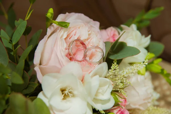 Fede nuziale in oro bianco. Due anelli di platino degli sposi e un mazzo di rose rosa e fiori bianchi — Foto Stock