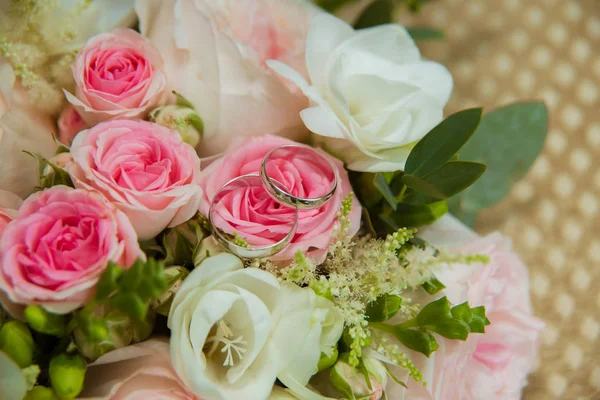 Γαμήλιο δαχτυλίδι σε λευκό χρυσό. Δύο δαχτυλίδια λευκόχρυσου η νύφη και γαμπρός και ένα μπουκέτο από τριαντάφυλλα ροζ και λευκά λουλούδια — Φωτογραφία Αρχείου