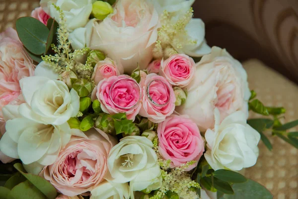 Sortija de boda en oro blanco. Dos anillos de platino de la novia y el novio y un ramo de rosas rosadas y flores blancas — Foto de Stock