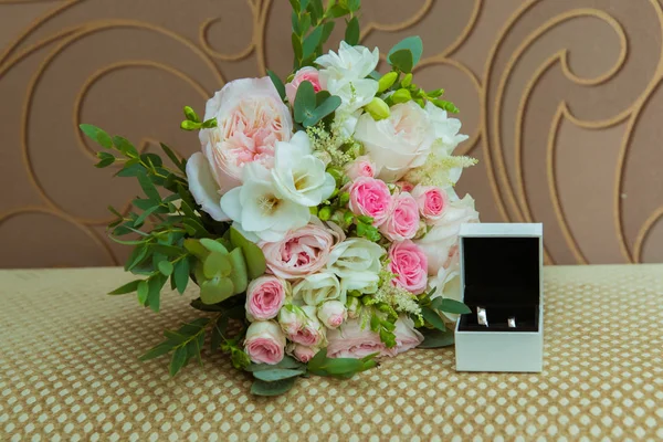 Sortija de boda en oro blanco. Dos anillos de platino de la novia y el novio en una caja blanca y un ramo de rosas rosadas y flores blancas — Foto de Stock
