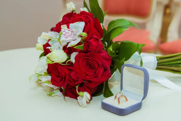 Obrączkę. Dwa złota vintage pierścionki panny młodej i pana młodego z diamentami są w niebieskie pole i bukiet czerwonych róż i białych kwiatów — Zdjęcie stockowe
