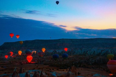 Kapadokya, Göreme, Anadolu, Türkiye. Dağların üzerinden uçan sıcak hava balonları günbatımı Cappadocia manzara. Turistler için en sevdiğiniz eğlencelerin.