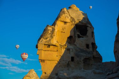 Göreme, Kapadokya Anadolu, Turkey: Eski taş evleri ve balon Göreme güneşli havalarda mavi gökyüzünde karşı. Sıcak hava balonu turistler için popüler bir uçuş olduğunu