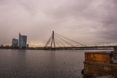 Riga, Letonya: Gökdelenler arkasında dur. Güzel sonbahar manzara. Nehir ve bulutlu havalarda köprü görünümü.