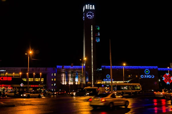 RIGA, LETTONIE : Grande horloge au sommet de la gare centrale de Riga. Paysage nocturne avec éclairage . — Photo