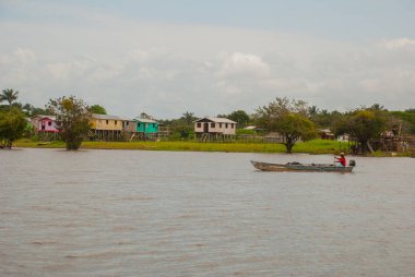 Amazon nehri, Amazonas, Brezilya: Teknede dans eden balıkçı. Ahşap yerel kulübeler, Brezilya'da Amazon nehri üzerinde evler.