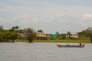 Amazon nehri, Amazonas, Brezilya: Teknede dans eden balıkçı. Ahşap yerel kulübeler, Brezilya'da Amazon nehri üzerinde evler.