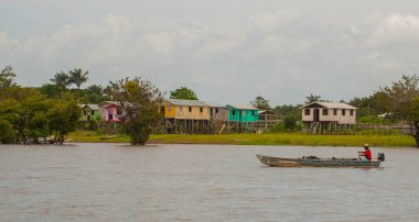Amazon nehri, Amazonas, Brezilya: Teknede dans eden balıkçı. Ahşap yerel kulübeler, Brezilya'da Amazon nehri üzerinde evler.