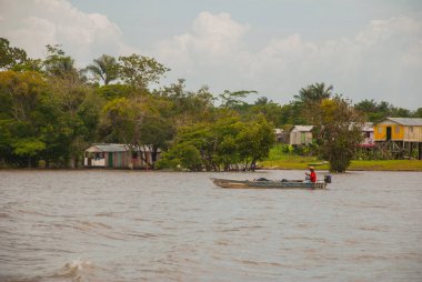 Amazon nehri, Amazonas, Brezilya: Teknede dans eden balıkçı. Ahşap yerel kulübeler, Brezilya'da Amazon nehri üzerinde evler.