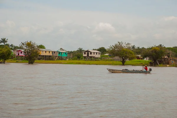 Amazon nehri, Amazonas, Brezilya: Teknede dans eden balıkçı. Ahşap yerel kulübeler, Brezilya'da Amazon nehri üzerinde evler.