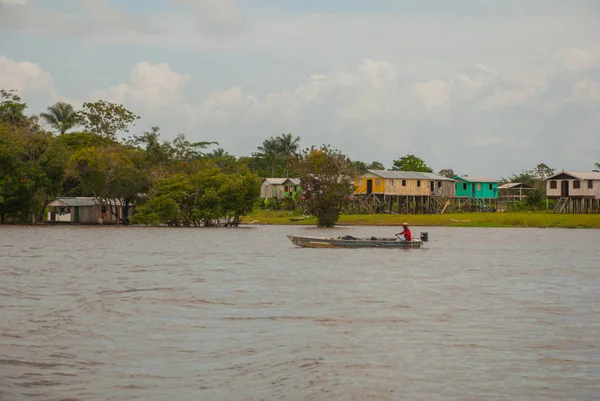 Amazon nehri, Amazonas, Brezilya: Teknede dans eden balıkçı. Ahşap yerel kulübeler, Brezilya'da Amazon nehri üzerinde evler.