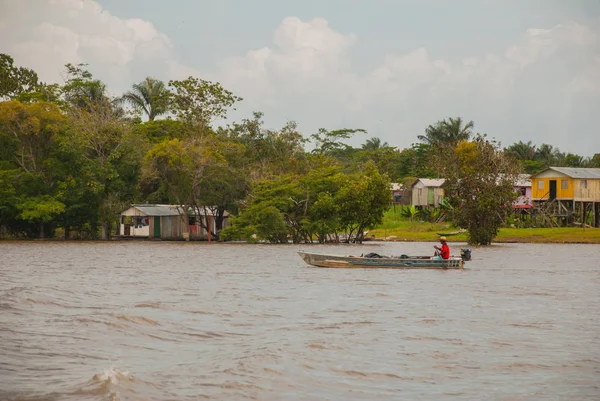 Amazon nehri, Amazonas, Brezilya: Teknede dans eden balıkçı. Ahşap yerel kulübeler, Brezilya'da Amazon nehri üzerinde evler.