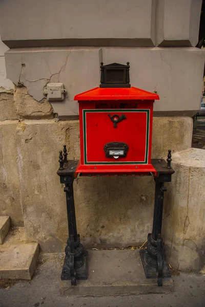 布达佩斯，匈牙利。明亮的红色邮箱，带有信件插槽，带有邮件喇叭的浮雕图像，有支腿支撑 — 图库照片