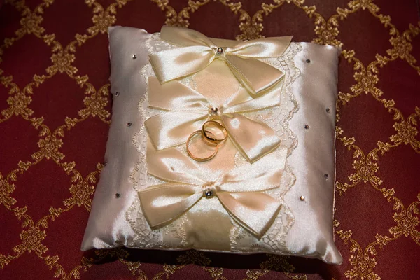Trauringe liegen auf einem weißen Kissen und trauriger Brautstrauß. — Stockfoto