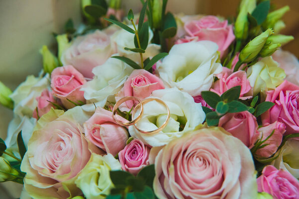 Beautiful delicate wedding bouquet of white and pink roses and wedding rings of the bride and groom.
