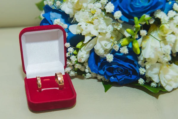 Vackra delikat bröllop bukett blå rosor och vigselringar av bruden och brudgummen i en röd låda — Stockfoto