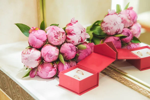 Hermoso ramo de boda delicado de peonías rosadas y anillos de boda de la novia y el novio en una caja roja — Foto de Stock