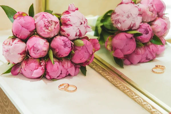 Hermoso ramo de boda delicado de peonías rosadas y anillos de boda de la novia y el novio . — Foto de Stock