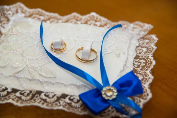 Belos anéis de casamento estão em um travesseiro com rendas brancas e trança azul . — Fotografia de Stock