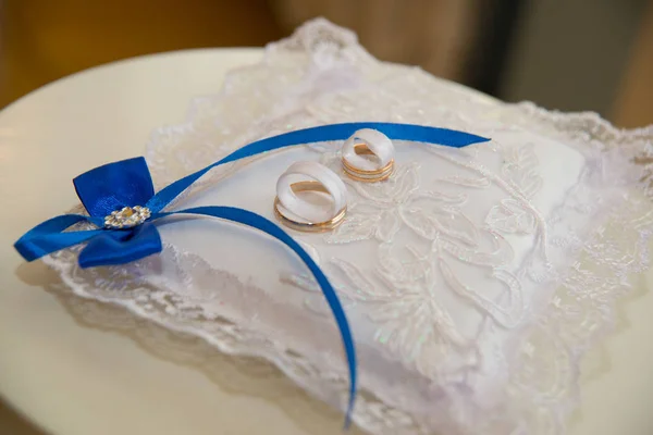 Belle fedi nuziali si trovano su un cuscino con pizzo bianco e nastri blu sotto forma di un fiocco . — Foto Stock