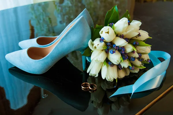 Wedding rings of the bride and groom on a Beautiful wedding bouquet of white tulips. Blue wedding shoes — Stock Photo, Image