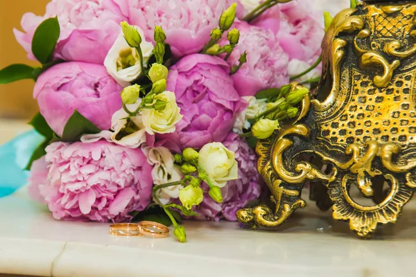 Hermoso ramo de boda delicado de peonías rosadas y anillos de boda de la novia y el novio . — Foto de Stock