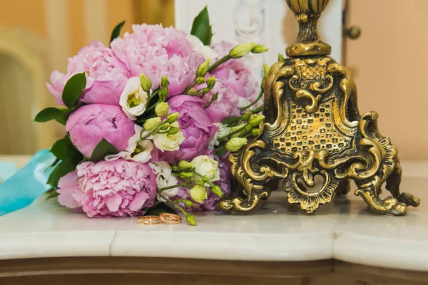 Hermoso ramo de boda delicado de peonías rosadas y anillos de boda de la novia y el novio . — Foto de Stock