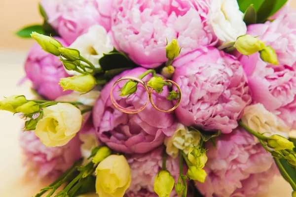 Hermoso ramo de boda delicado de peonías rosadas y anillos de boda de la novia y el novio . — Foto de Stock
